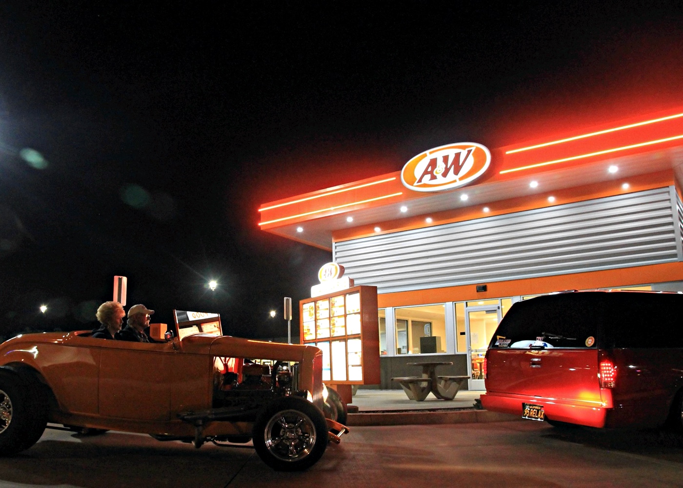 Two cars in A&amp;amp;W Restaurant drive-thru during the nighttime. 