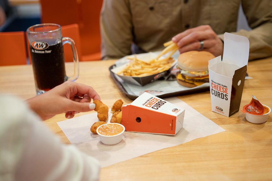 Two people at table with cheese curds, mug of Root Beer, cheeseburger, and fries