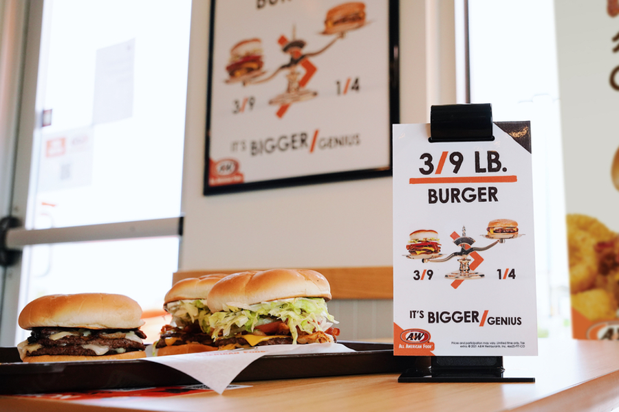 Photo of two burgers sitting on a table in an A&W Restaurant. A table tent that says "3/9 lb. Double Burgers" is on the right side.