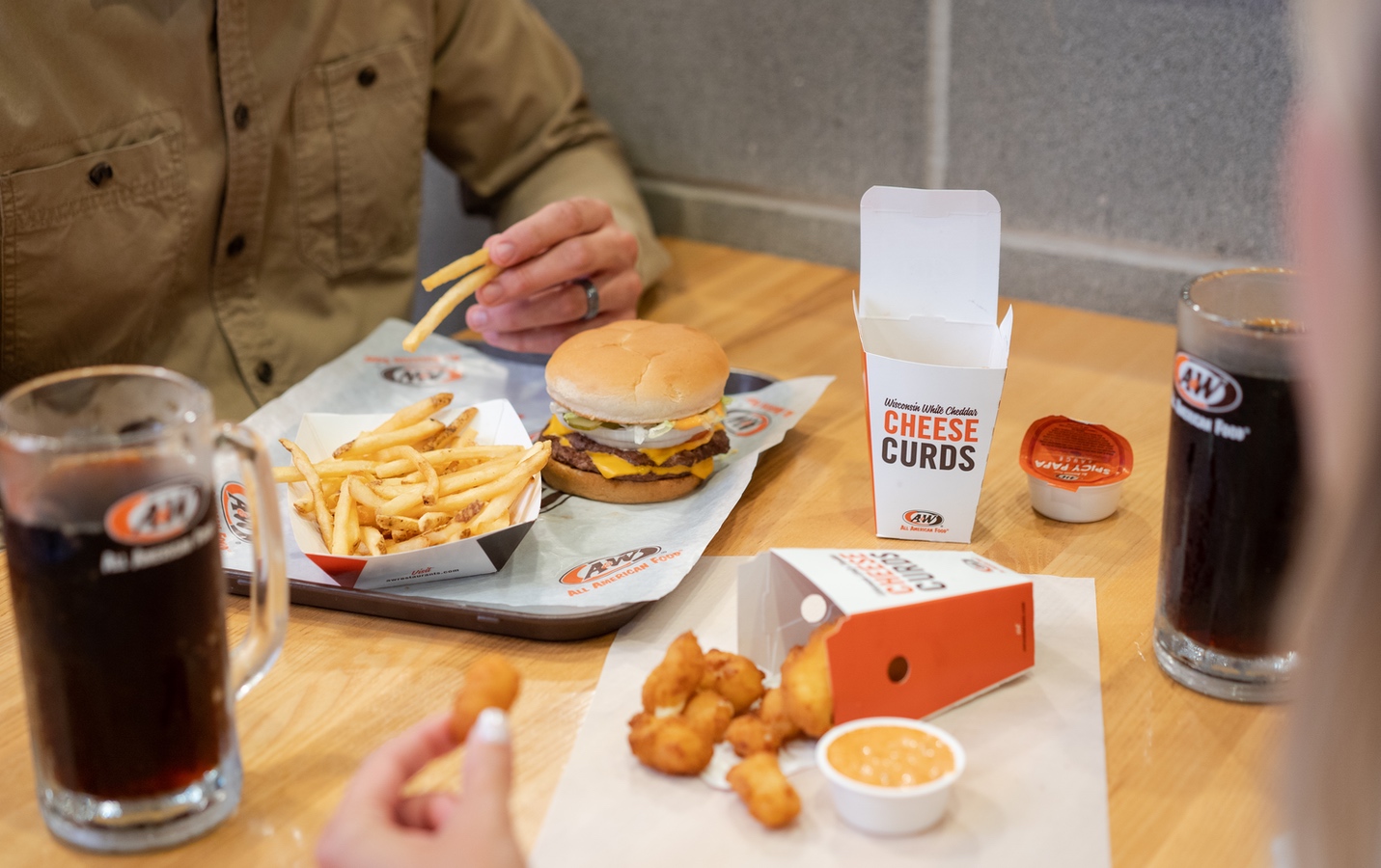 Two people at a table with mug of Root Beer, Burger, Fries, Cheese Curds